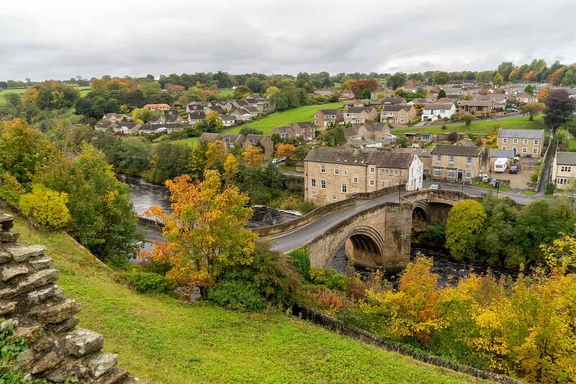 Aerial view of Barnard Castle in County Durham showing the stone bridge over the River Tees surrounded by autumn trees and village houses.