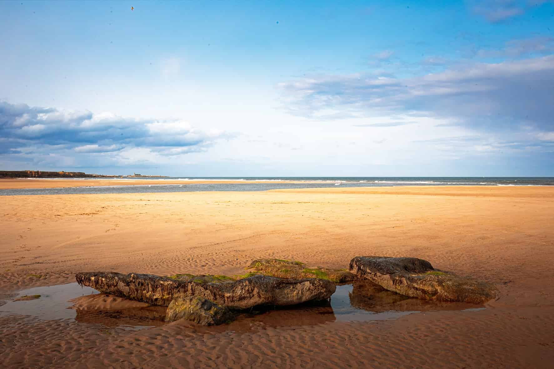 Full Fibre Broadband in Northumberland Wide view of Cambois Beach in Northumberland with golden sand, coastal rocks and the North Sea under a bright blue sky.