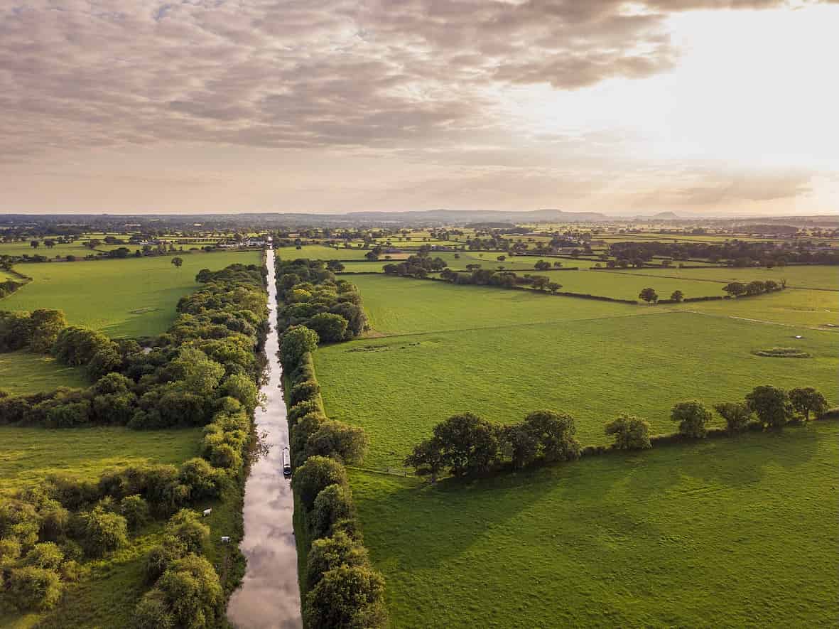 Full Fibre Broadband in Cheshire Villages | Fusion Fibre Group  Aerial view of the Cheshire countryside with a canal running through green fields and farmland under a soft evening sky.