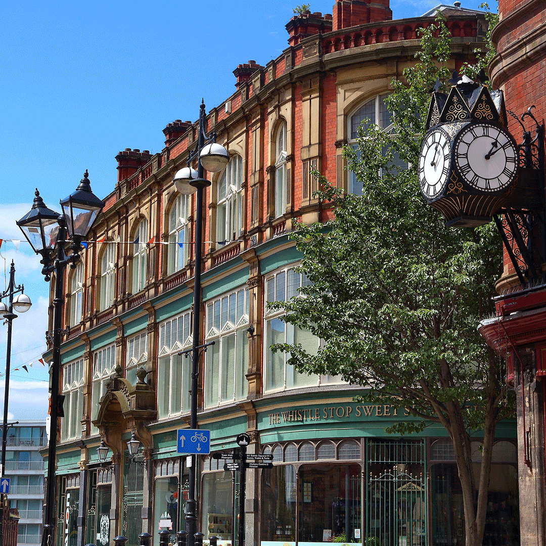 Historic town centre in Rotherham with Victorian architecture, shopfronts, and street clock on a sunny day.