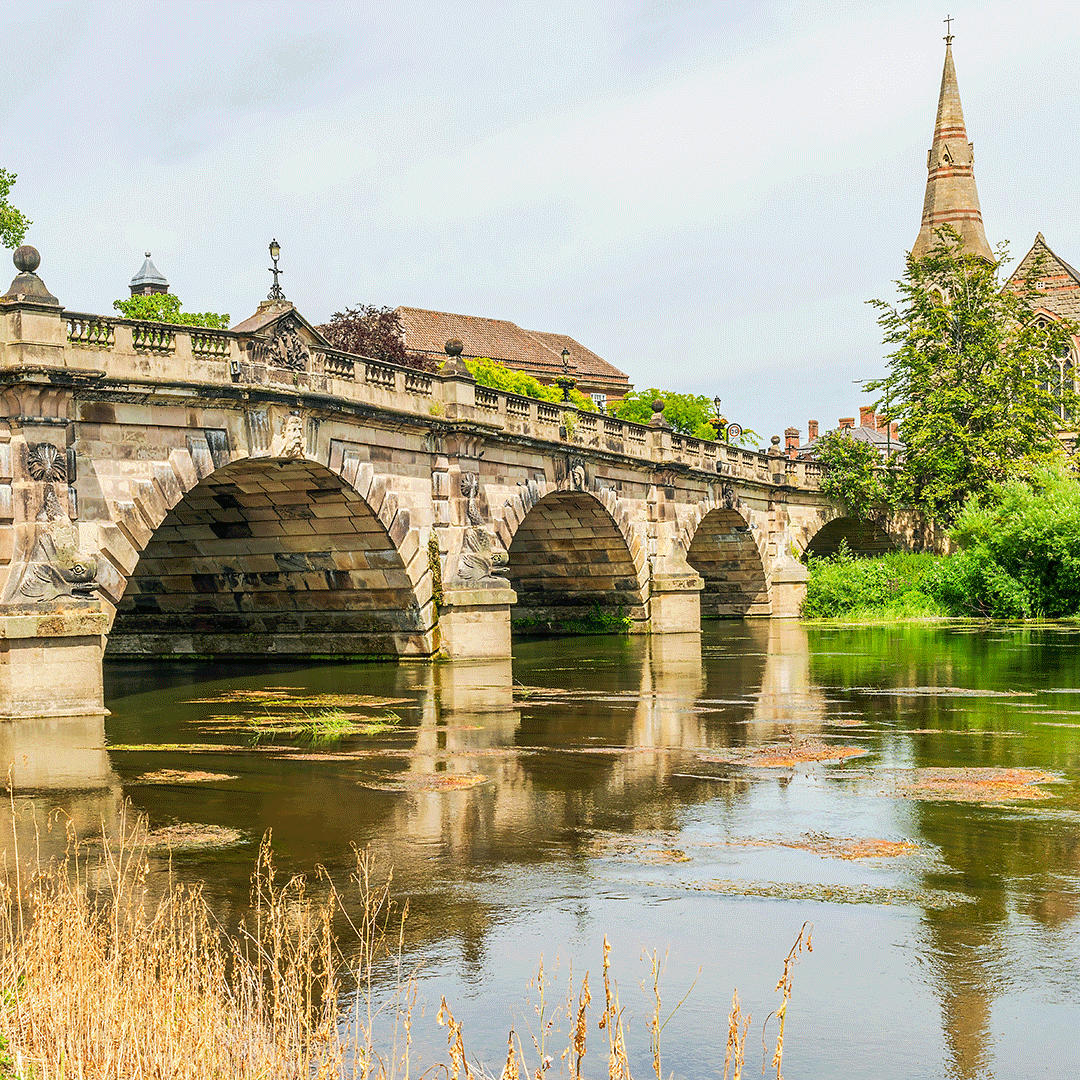 Historic stone bridge over the River Severn in Shrewsbury, Shropshire, with church spire in the background.