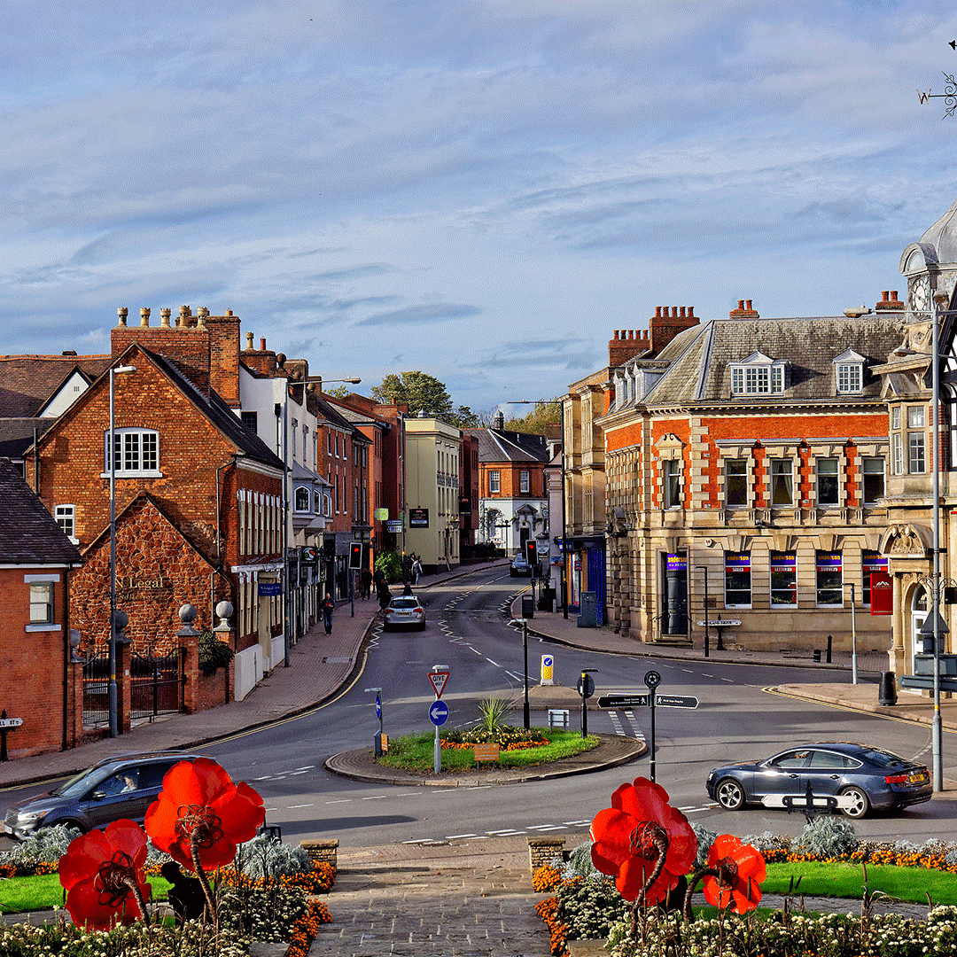 Street view of Sutton town centre in London Borough of Sutton with historic buildings, cars, and flower displays.